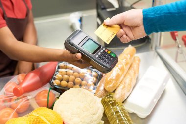 Yiyecek ürünlerine kredi kartıyla ödeme yapan erkek tüketici, ödeme terminali üzerinden tezgah üzerinden elinde tutuyor.