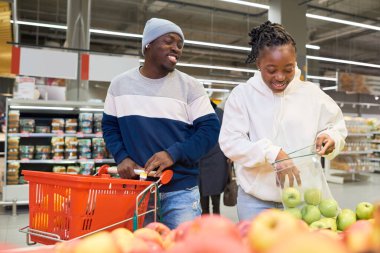 Genç ve mutlu Afro-Amerikan zoomerlar taze meyve seçerken süpermarketin bakkal bölümünde sergileniyor.