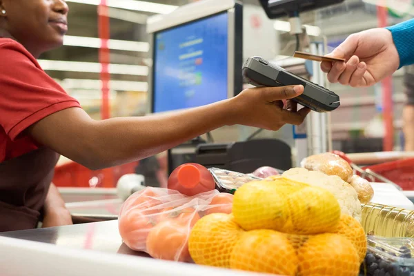 購入者がスーパーで食品を購入する際にクレジットカードを保持しながら 決済端末を保持している若い黒人女性 — ストック写真