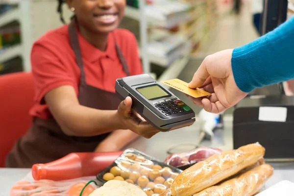 スーパーで食品を買いながら若い笑顔ショップアシスタントが保有する端末決済上でクレジットカードを保有する購入者 — ストック写真