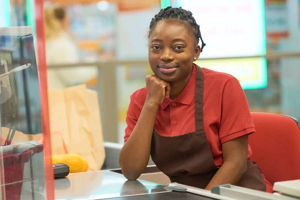 Jovem Vendedora Bem Sucedida Uniforme Sentada Balcão Caixa Supermercado Olhando — Fotografia de Stock