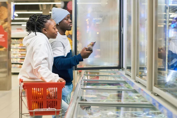 Pareja Joven Con Carrito Compras Eligiendo Productos Alimenticios Congelados Supermercado — Foto de Stock