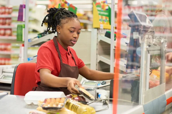 Młoda Czarna Kobieta Mundurze Skanuje Pakowane Produkty Spożywcze Kupujących Siedząc — Zdjęcie stockowe