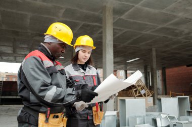 İki ciddi ırklar arası mühendis inşaat sahasında dikilirken planlarını planlıyorlar.