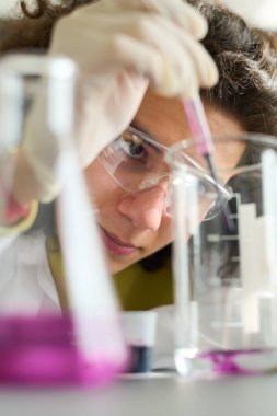 Koruyucu gözlüklü ergen adam kimyasal deney sırasında bardağa veya tüpe şeffaf sıvıyla mor sıvı madde bırakıyor.