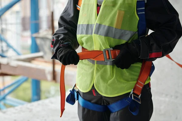 身穿手套和反光背心的年轻建筑工人在准备工地建筑工程时 将安全带系在腰部 — 图库照片