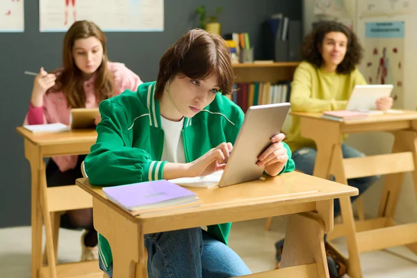 年轻的女学生穿着便服 一边看平板电脑的屏幕 一边在网上浏览同学们的课堂提示 — 图库照片