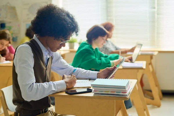 在解剖学课上 一个拿着平板电脑的少年坐在课桌前完成个人作业的侧视图 — 图库照片