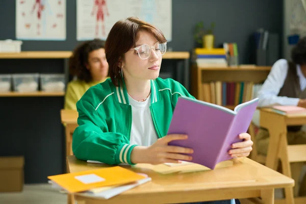一个严肃的女学生坐在课桌前和两个男同学对着干 一边翻阅抄本上的笔记 — 图库照片