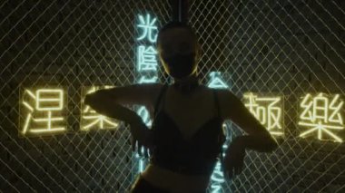 Kafası kazınmış, yüzü siyaha boyanmış, stüdyoda elleri ve vücudu hiyeroglifler şeklinde neon ışıkları olan, nirvana ve batı cenneti anlamına gelen ışıklar seğiren bir kız.