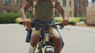 Sıcak bir yaz günü bisiklete binen iki beyaz ve Afrikalı Amerikalı çocuğun mutlu bir şekilde gülüp sohbet ederken orta eğik çekimleri.