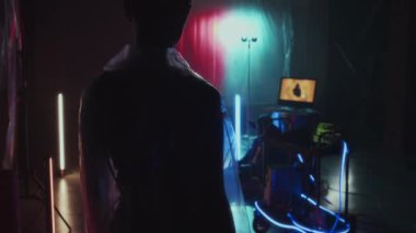 Kafası tıraşlı, şeffaf su geçirmez ceketli, duvarlarında plastik film, bilgisayarlar ve neon ışıklarla saklanan siber punk kızın arka silueti.