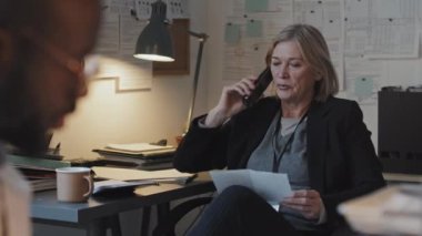 Resmi takım elbiseli, olgun sarışın, beyaz kadın savcının orta derecede yavaş bir temposunda ofiste oturuyor, telefonla konuşuyor, sonra da kameraya bakıyor.