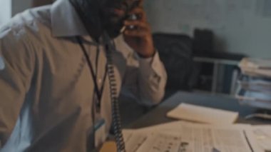 Gözlüklü ve resmi gömlekli genç Afro-Amerikan ajanının yavaş çekimde ofiste oturması ve telefonda konuşması.
