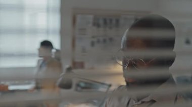 Genç Afro-Amerikan erkek ajanın ofisteki kapaktan profesyonel kameraya çektiği yatay jaluzilerle göğüs yukarı bakış açısı.