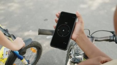 Pusula uygulamalı akıllı telefonu tutan koyu tenli çocuğun yüksek açılı yakın plan fotoğrafı ve aşağıda bisiklet gidonu var.