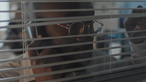 Close Young African American Man Eyeglasses Peeking Horizontal Blinds Looking — Stock Video