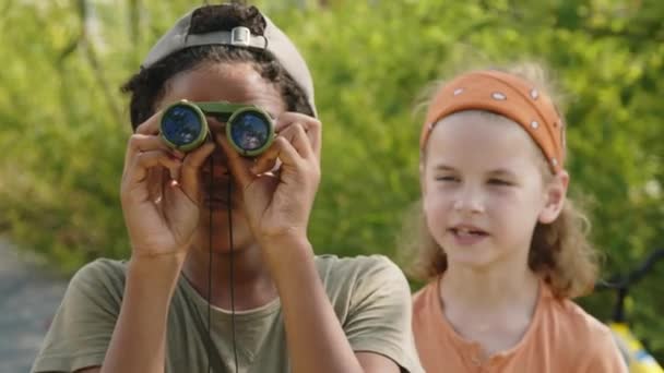 미디엄 아프리카 미국인 아이는 쌍안경을 친구는 배경에 나무와 물체를 가리키고 — 비디오