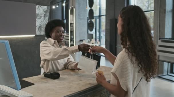中级非洲裔美国人销售员给漂亮的女客户带着珠宝的黑白购物袋 这些女客户用信用卡付款 微笑着离去 — 图库视频影像