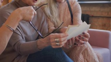 Yazılı eski fotoğraflara bakarken, gençliği ve güzel zamanları hatırlayan üç neşeli olgun kadın konuşuyor.