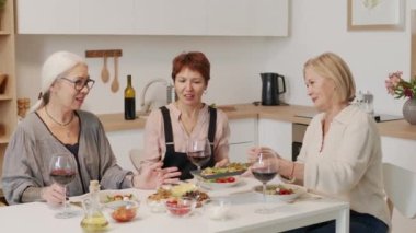 Üç yetişkin kadın en iyi arkadaş mutfak masasında birlikte oturup, aperatiflerle şarap içip sohbet ediyorlar.