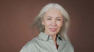 Uzun gri saçlarıyla kameraya gülümseyen çekici yetişkin bir kadının göğüs portresi.