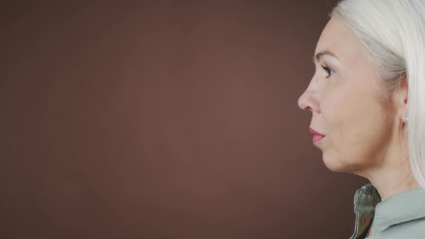 站在棕色背景上的白种人长而直的白发女子的侧景画室肖像 — 图库视频影像