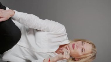 Stüdyoda sandalyede otururken kameraya poz veren kendinden emin beyaz iş kadınının dikey portresi.