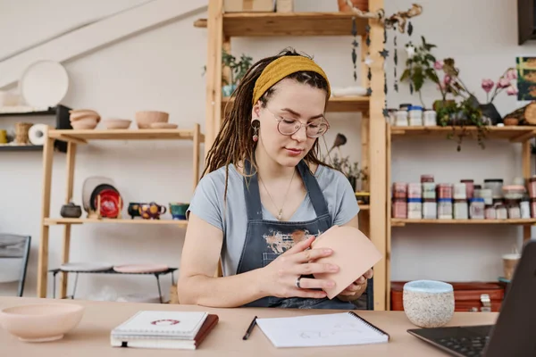 在小商店或工作室工作时 年轻的有创意的女商人穿着便服 一边拿着陶器 一边评价陶器的质量 — 图库照片