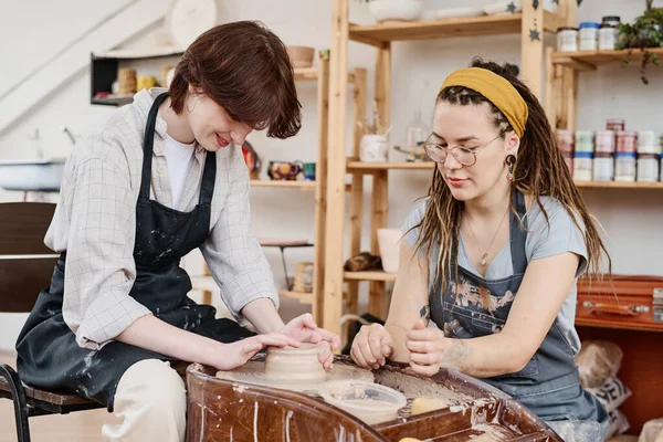 回転する車輪や新しい鍋やその他の土器アイテムを作成する作業服に座っている陶器のコンサルティングの女の子の若い女性のマスター — ストック写真
