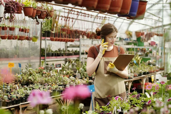 花き市場に立つ携帯電話による注文の受諾中に彼女の手にクリップボードを見て作業服の女性庭師 — ストック写真