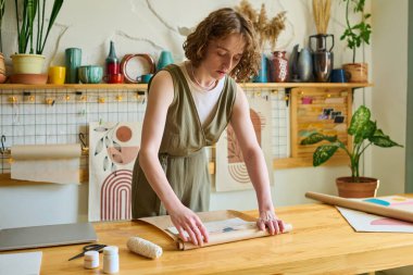 Genç bayan tezgahtar atölyedeki müşteri siparişini paketlerken soyut resmi kağıda sararken masanın üzerine eğilmiş.