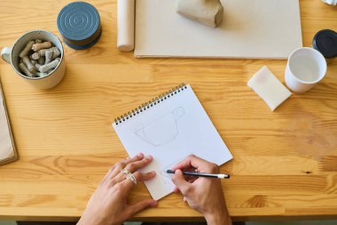 Genç zanaatkârların ya da zanaatkarların el açısının üzerinde tahta masa ile çalışırken not defterine yeni bir toprak eşyası çizimi yapılıyor.