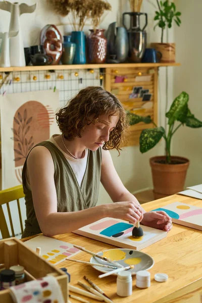 ワークショップで新しい抽象絵画を研究しながら 紙の上に色を適用するためにスポンジを使用してカジュアルウェアの創造的な女性アーティスト — ストック写真