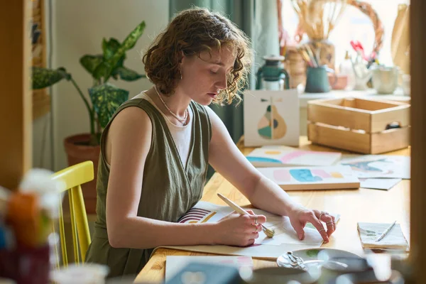 严肃的年轻女性 带着画笔坐在工作室的工作场所旁边 在纸上用水彩画抽象的东西 — 图库照片
