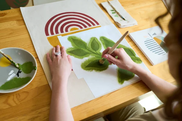 机の上に座りながら 絵筆とガッシュで緑の葉を描く美術学校の女子学生の手 — ストック写真