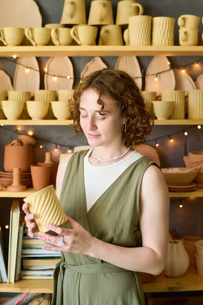 陶器で展示され 贈り物を選ぶことによって立っている間 彼女の手で手作りの粘土マグカップを見て犠牲者の若い女性 — ストック写真