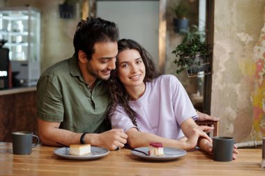 Romantik öğle yemeği sırasında sevgilisinin yanında oturmuş kahvesini yudumlarken kameraya bakan genç bir kadın.