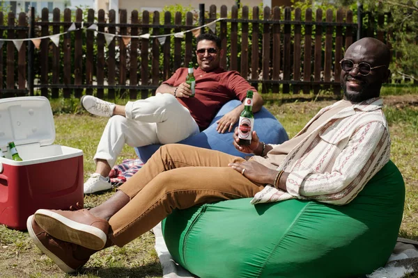 Twee Gelukkige Jonge Interculturele Mannen Met Flesjes Bier Zittend Zakkenstoelen — Stockfoto