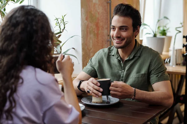 一个面带微笑的年轻人和他的女朋友坐在桌旁喝咖啡 边喝卡布奇诺边聊天 — 图库照片
