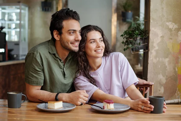 年轻貌美的情侣们坐在舒适的咖啡店的餐桌旁 一边看着窗外 一边吃着美味的加卡布奇诺芝士蛋糕 — 图库照片