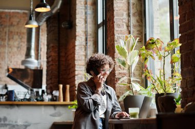 Modern kafe danışmanlık müşterilerinin mutlu genç bayan sahibi telefondaki ve internetteki büyük pencerenin önünde otururken