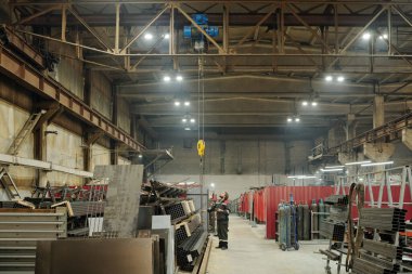 Endüstriyel makine veya diğer inşaat ekipmanlarını ayarlayan erkek mühendisin çalıştığı geniş bir fabrika atölyesi.