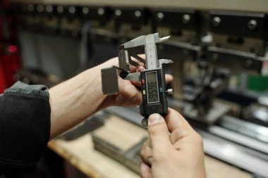 Erkek mühendis, iş yeri üzerinde küçük paslanmaz çelik detayları ve endüstriyel makinelerin yapımında kullanılan malzemelerle önlemler alıyor.