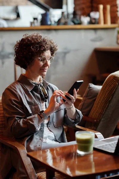年轻自信的女商人或自由职业者坐在咖啡店时 穿着便服 在智能手机里发短信或打滚 — 图库照片