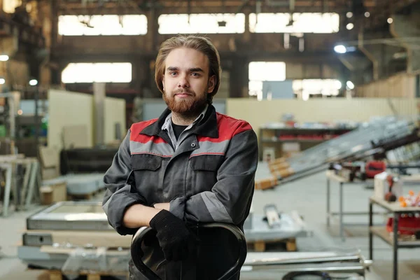 工場の内部に対してカメラの前に立っている間 胸の横に彼の腕を保つ作業服の若い自信のエンジニア — ストック写真