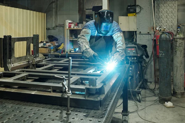 巨大な産業機械の金属部品を溶接しながら 彼の作業台の上に曲げ保護作業服の若い男性専門家 — ストック写真