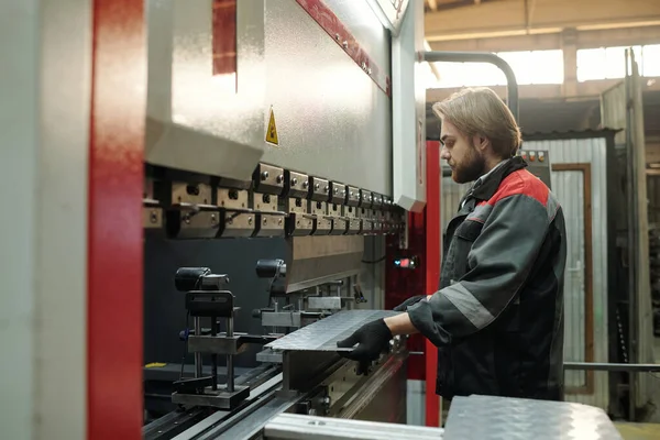 工場内の労働機械その他の設備の一部に金属板を用いた作業服の若手技術者の側面図 — ストック写真