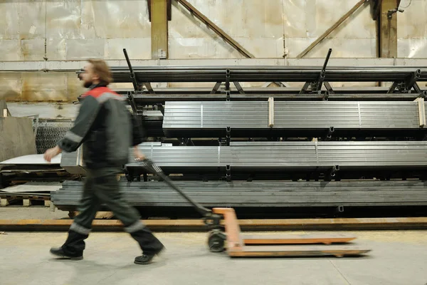 车间工装拉叉车通过堆叠金属板时男性工程师模糊轮廓的侧视图 — 图库照片