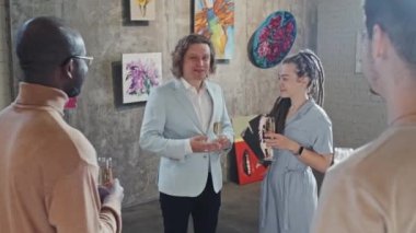 Orta büyüklükteki sanatçılar ve iş adamları ellerinde köpüklü şarapla modern sanat galerisinin açılışını kutluyorlar.